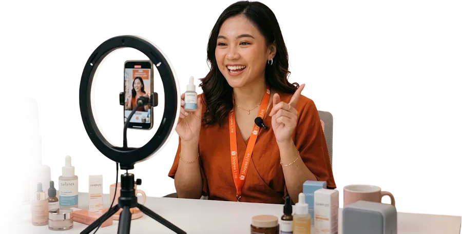 Host live selling tersenyum memegang produk perawatan kulit di depan ring light
